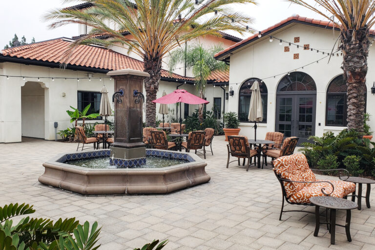 A courtyard with tables and chairs, fountain and palm tree.